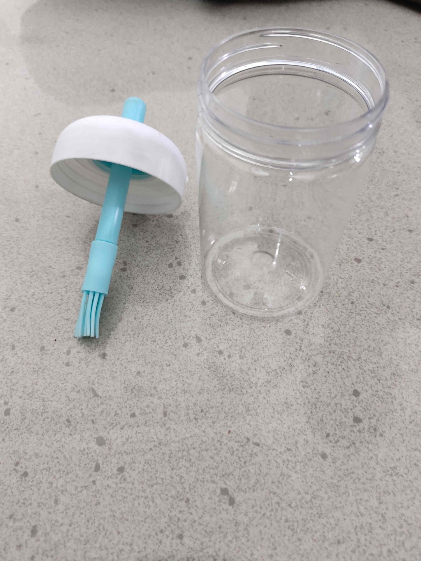 Clear plastic container with a white cap and blue brush on a gray surface