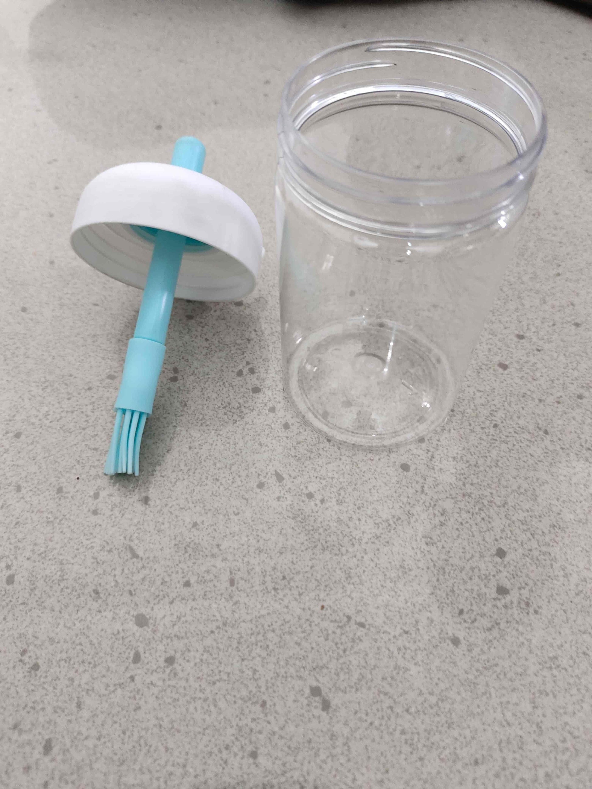 Clear plastic container with a white cap and blue brush on a gray surface
