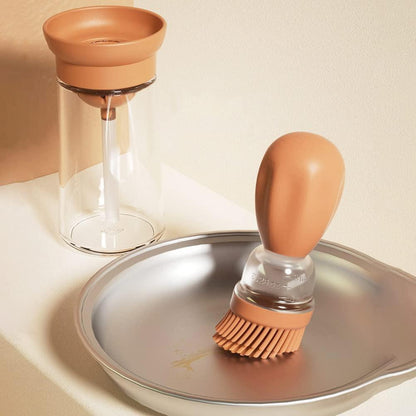 Baking brush with terracotta handle and bristle head on a metal surface, next to a glass container.