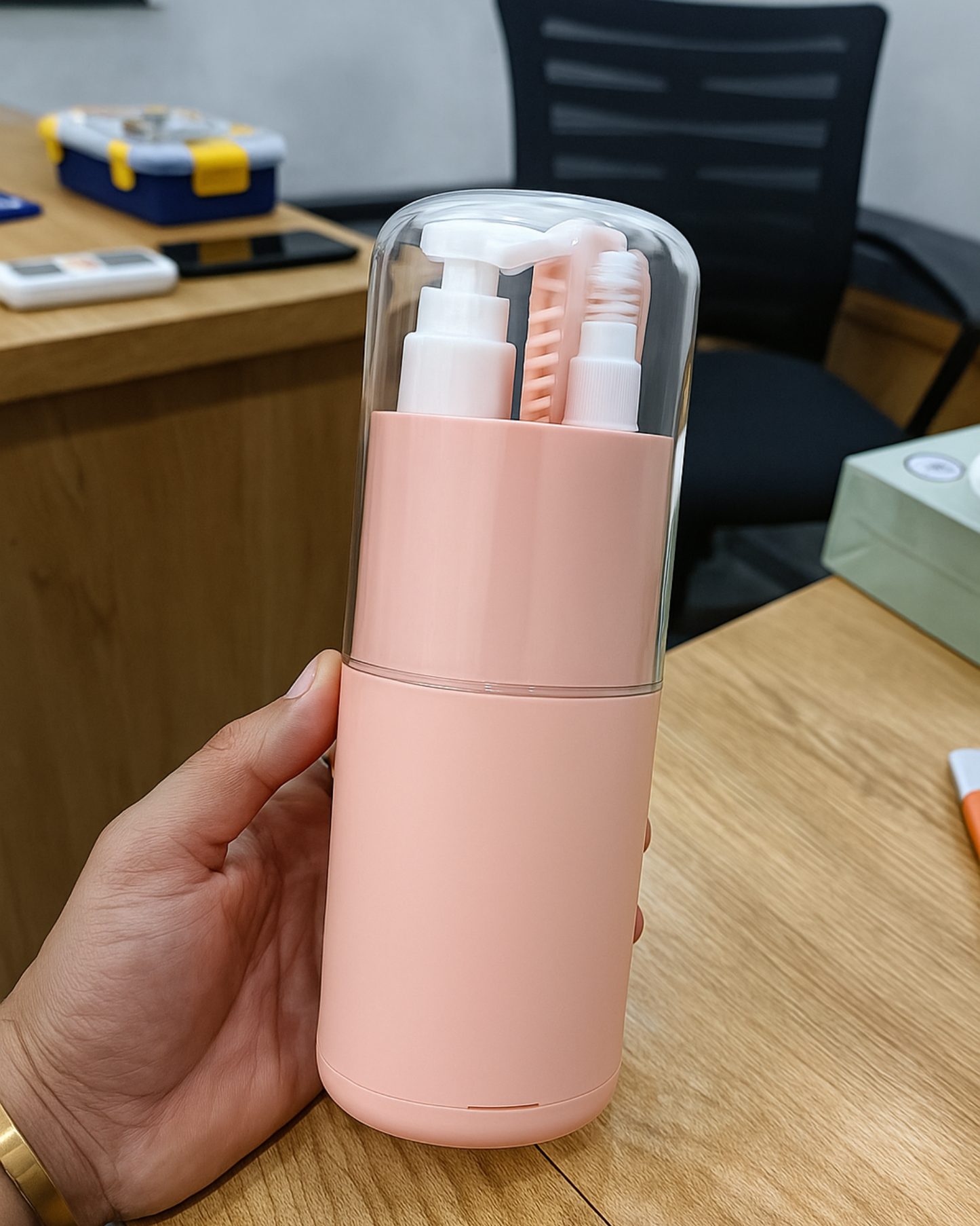 Pink travel container with multiple bottles on a wooden desk.