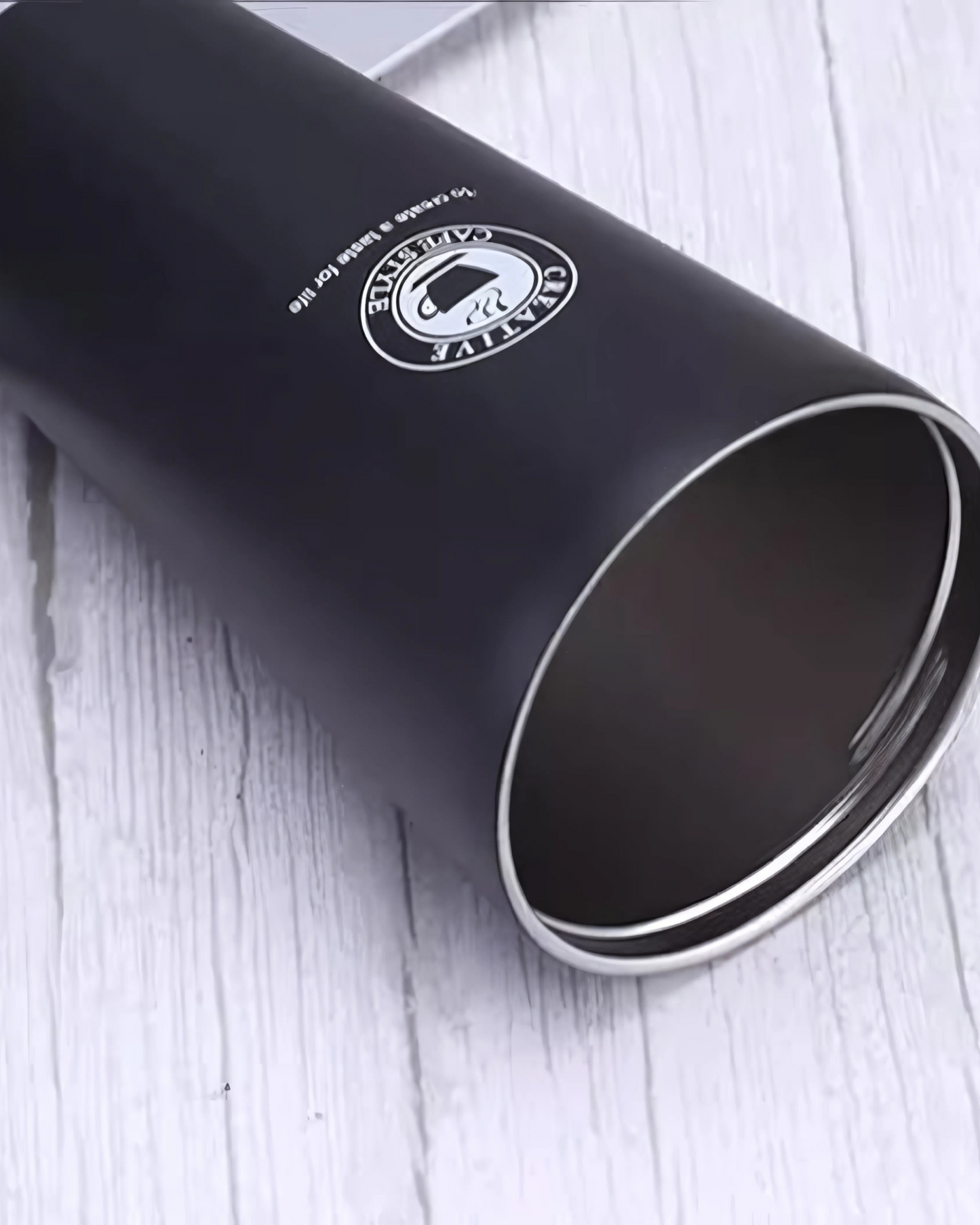 Close-up of a black tumbler with a logo on a white wooden surface.