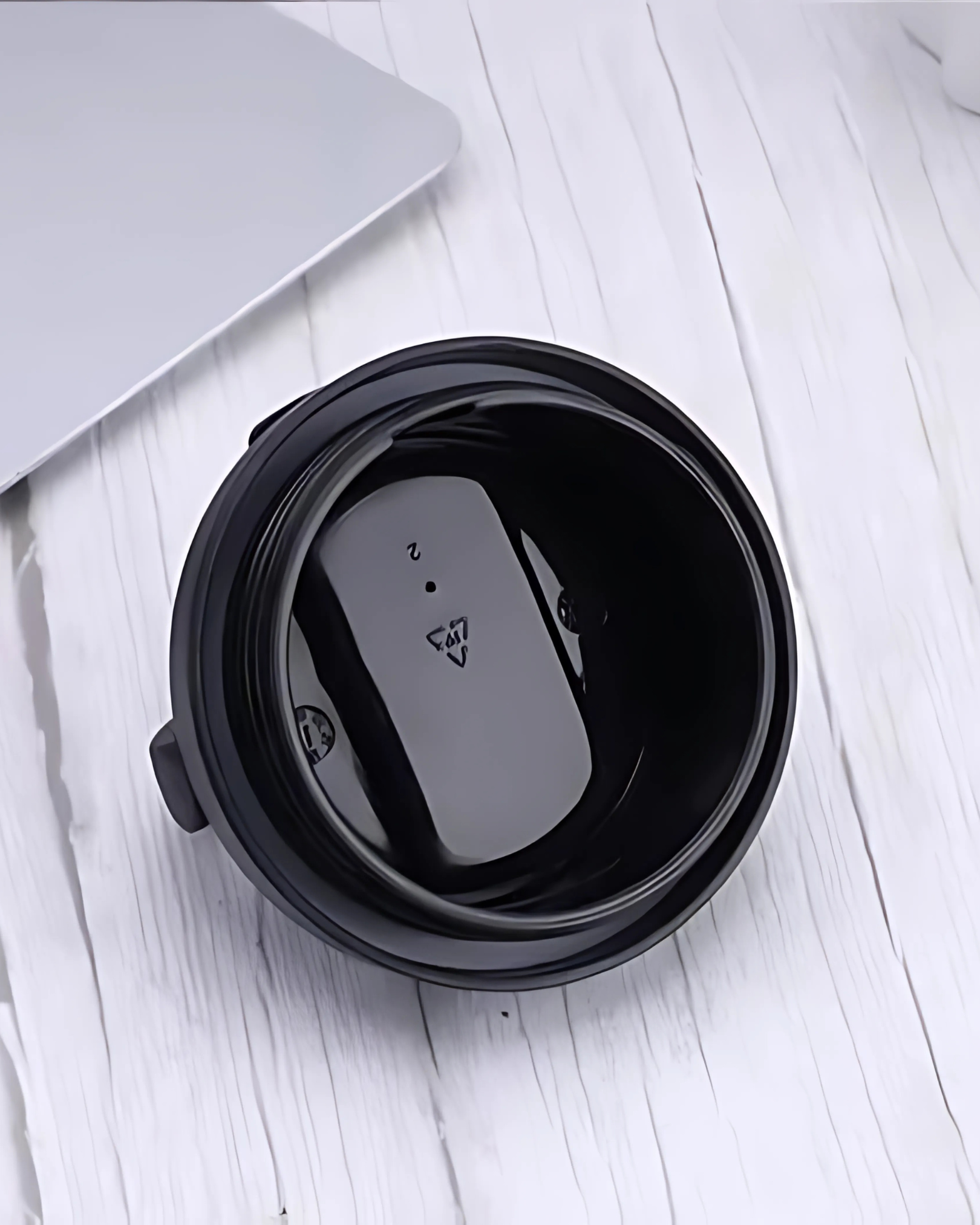 Black container with a white object inside on a light wooden surface