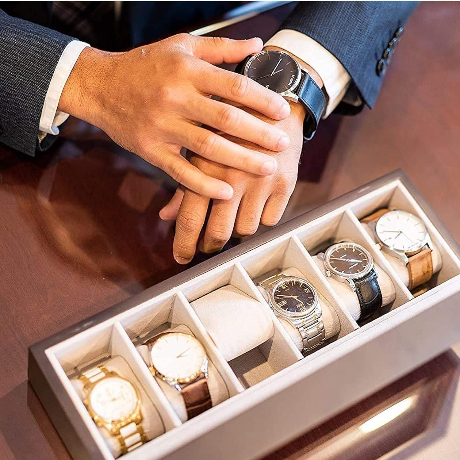 Man's hand holding a watch above a display box with various watches.