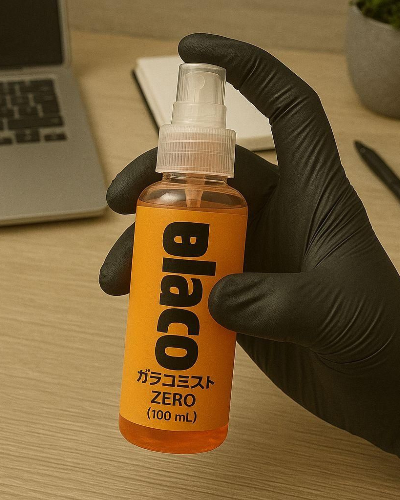 Hand wearing a black glove holding an orange bottle labeled 'blaco' on a desk.
