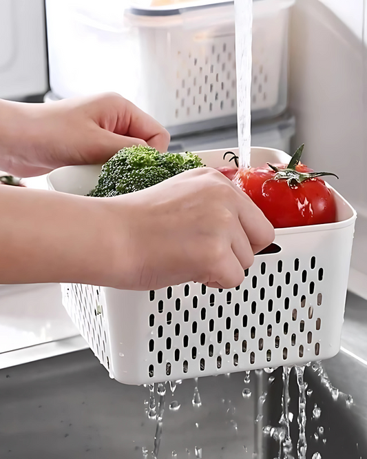 Person washing vegetables in a white colander under running water in a kitchen sink.