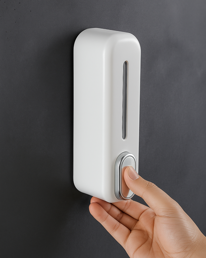 White wall-mounted dispenser with a hand pressing the button against a dark background.