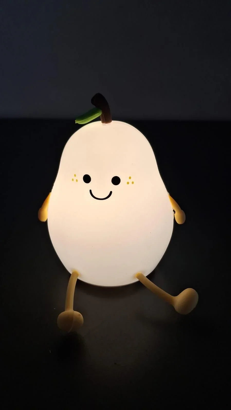 Plush pear-shaped night light with a smiling face on a black background