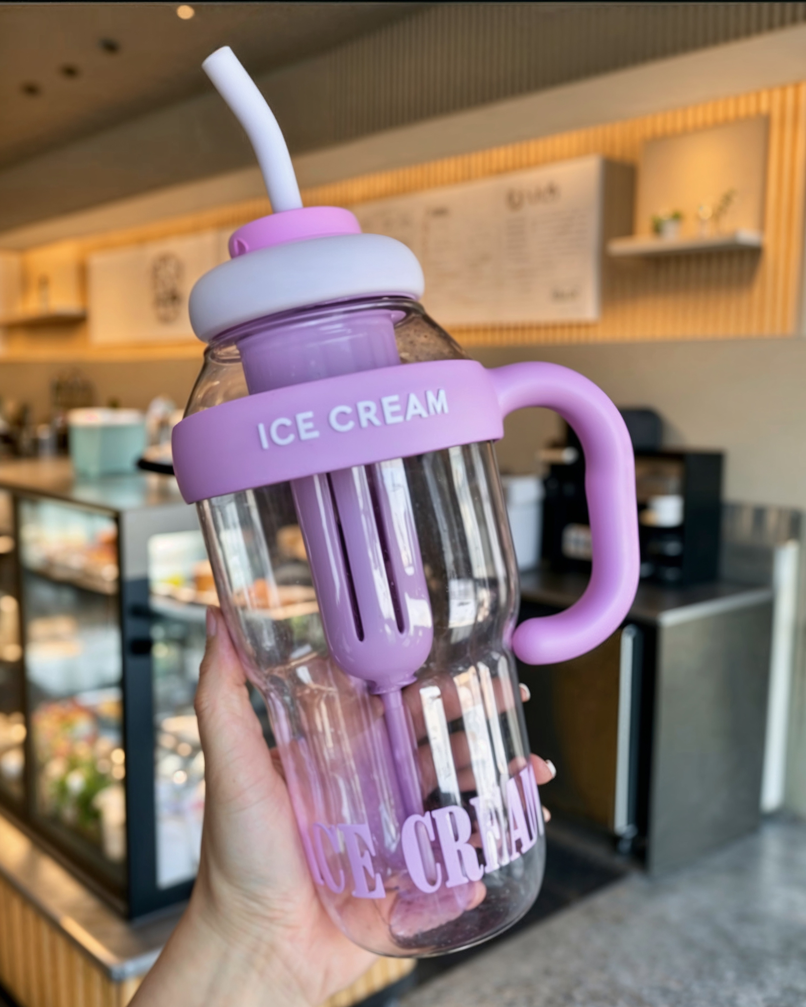 Purple ice cream-themed tumbler with handle and straw held in hand.