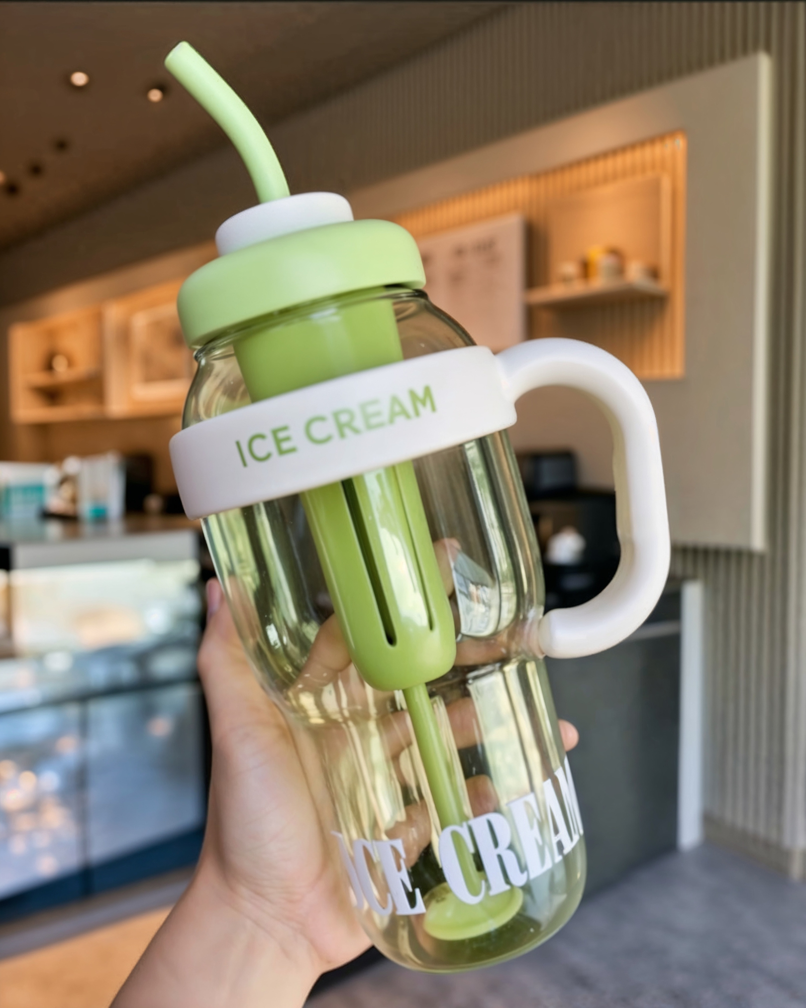 Green ice cream cup with handle and straw held by a hand.